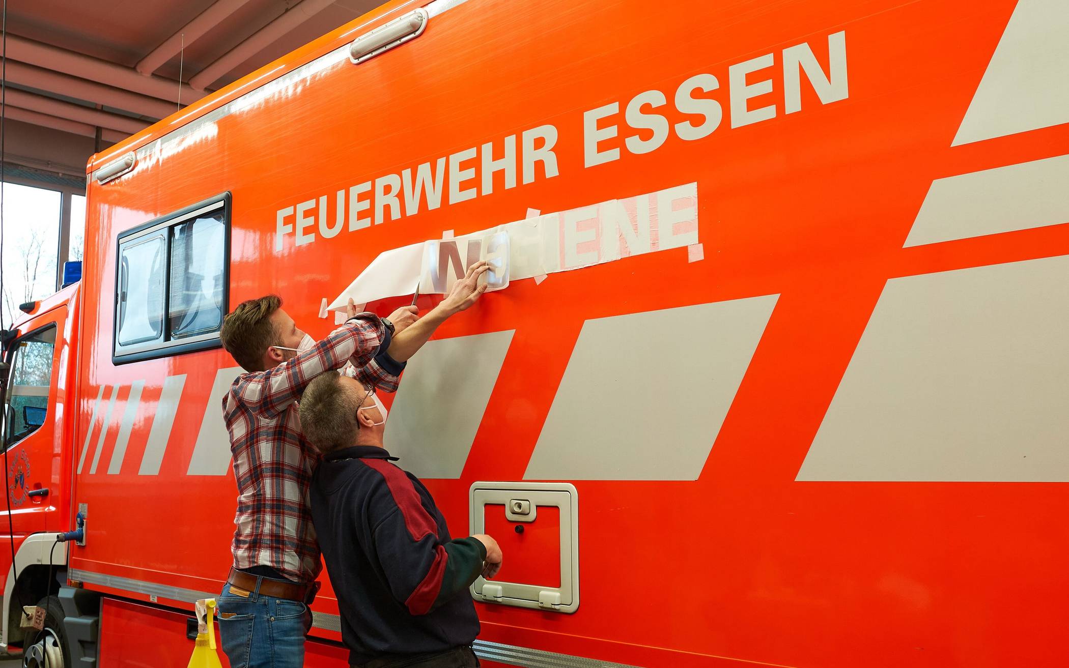  Mitarbeiter der Lebenshilfe Wuppertal beschriften einen Essener Feuerwehrwagen.  