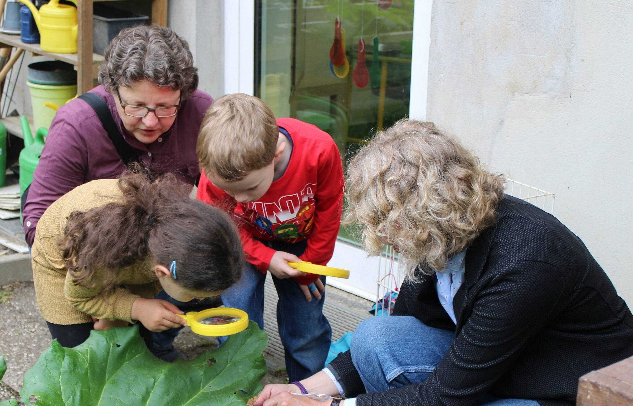  Anja Liebert (li.), Dr. Susanne Reinold (Netzwerkkoordinatorin „Haus der kleinen Forscher“) und die Kinder nehmen Blätter unter die Lupe. 