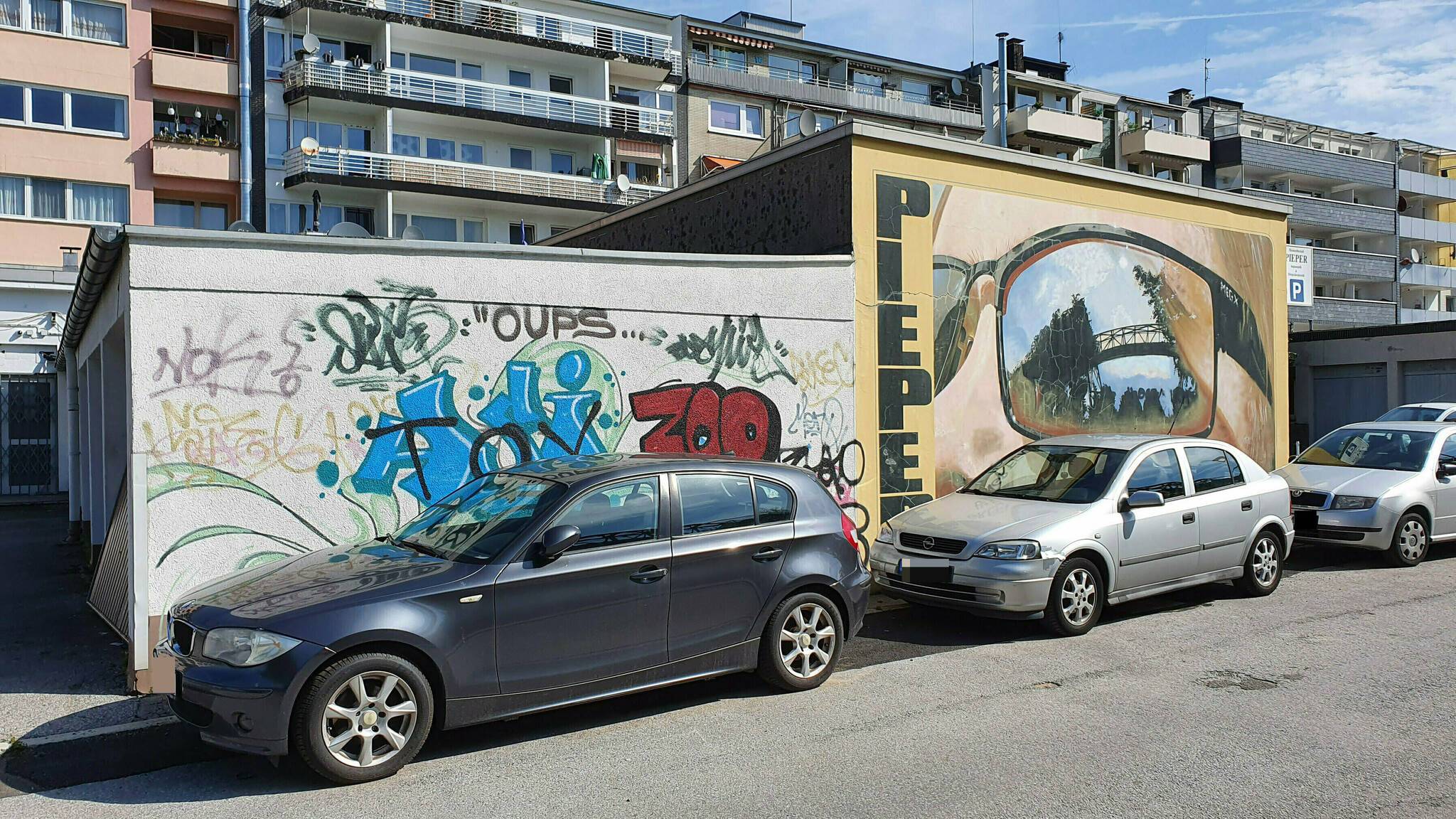  Das Wandbild von Martin Heuwold, vor 12 Jahren als private Initiative des Optikers Axel Pieper entstanden, bleibt erhalten und wird vom Künstler aufgefrischt. Der Betrachtende mit der Sonnenbrille, in der sich die Schwebebahn spiegelt, soll nun Gesellschaft von anderen Fassaden in gleich hoher künstlerischer Qualität bekommen. 