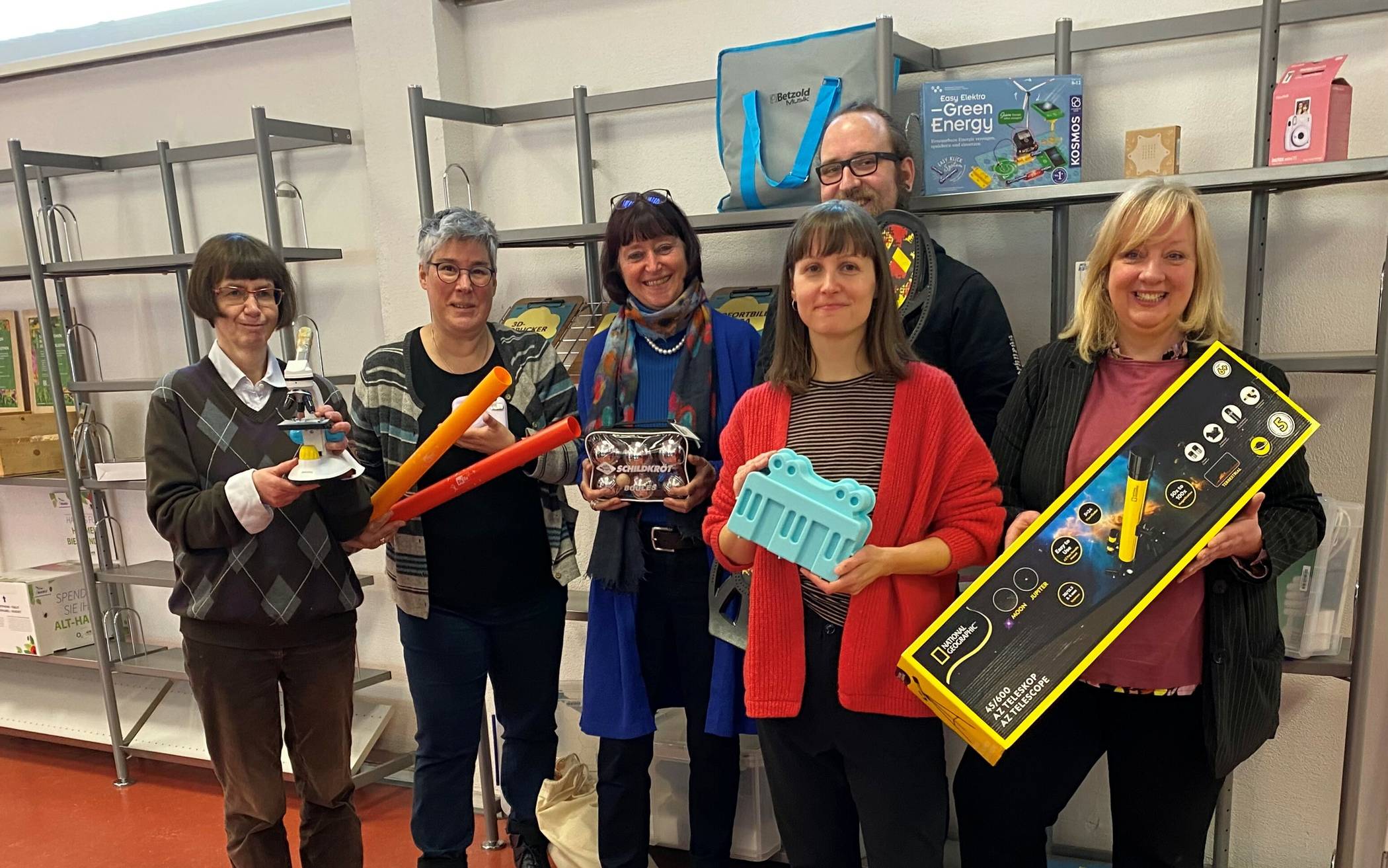 Das Projektteam der LeihBar präsentiert einige der Gegenstände, die ab sofort in der Zentralbibliothek ausgeliehen werden können. Im Vordergrund steht Projektleiterin Maria Musiol mit einer der fünf Schwebebahn-Backformen, die von der Plattform Wuppertal Online City für die LeihBar gespendet wurden. Hinter ihr von links nach rechts: Michaela Piel, zuständig für die in diesem Fall völlig neu zu gestaltende Katalogisierung, hält ein Lern-Mikroskop in der Hand. Neben ihr stehen Direktorin Cordula Gladrow, Susanne Hasenöhrl und Christian Brenscheidt sowie ganz rechts Vize-Direktorin Katja Schneider mit weiteren nützlichen Gegenständen für die Freizeitgestaltung.