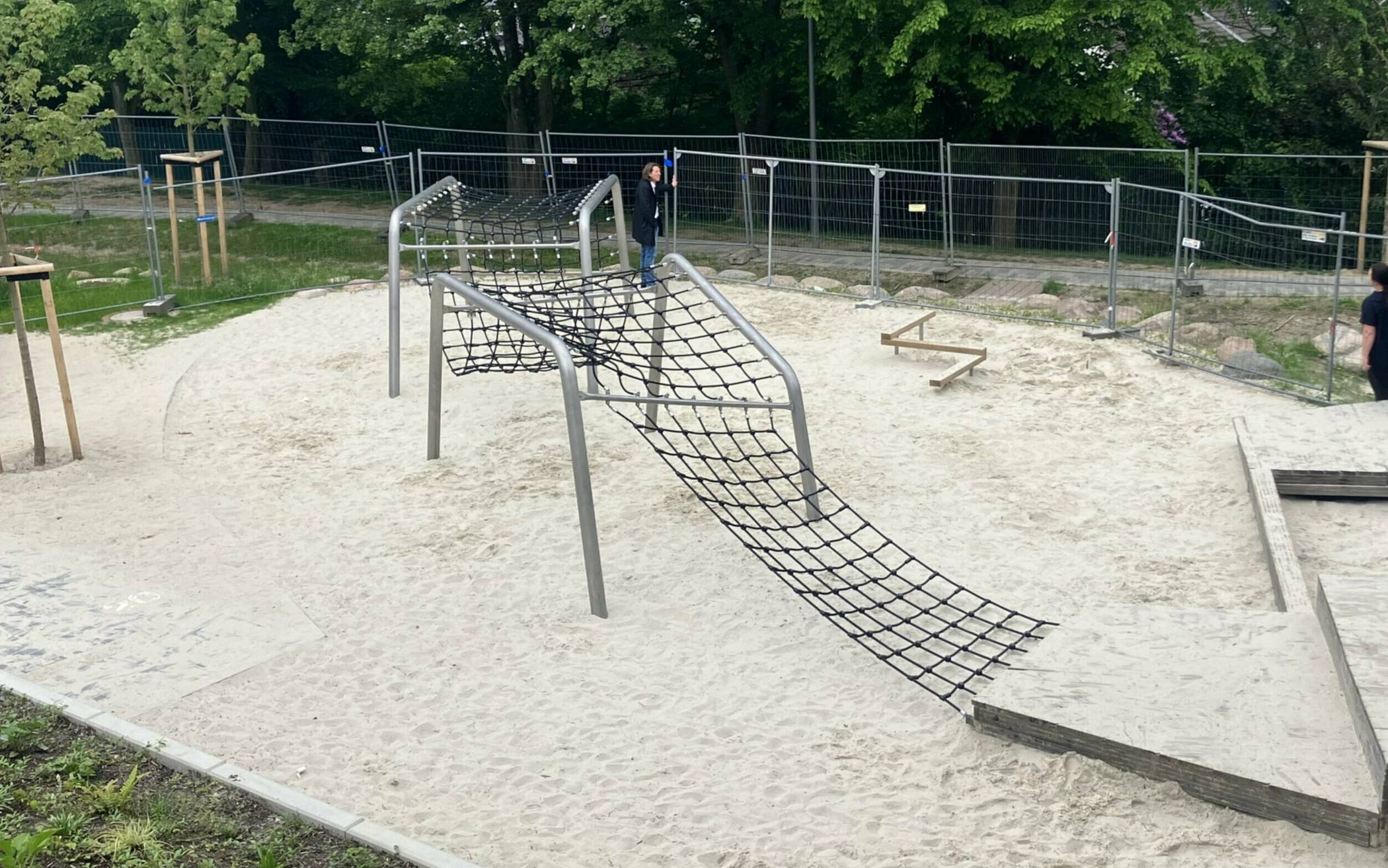 Die Eltern begutachten den kaputten Bauzaun, der Spielgeräte und Regenmulden trennt. 