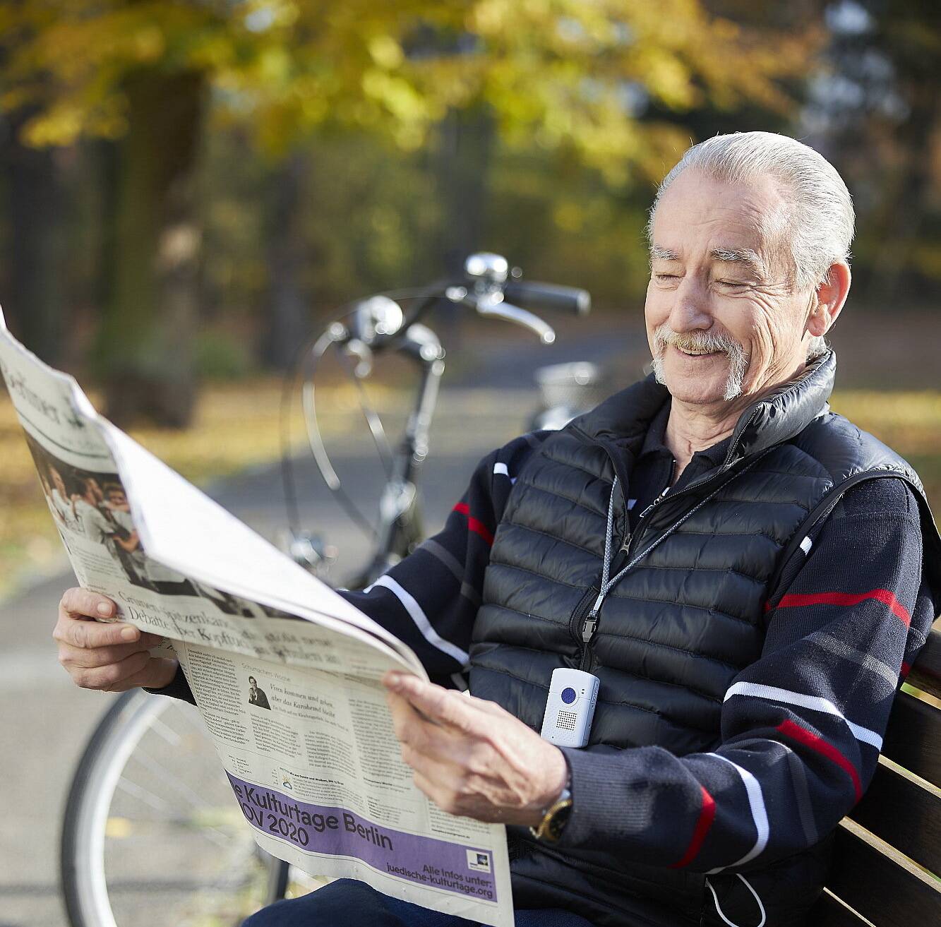  Der Kombinotruf funktioniert auch unterwegs: Ein älterer Mann trägt das Gerät im Freien. 
