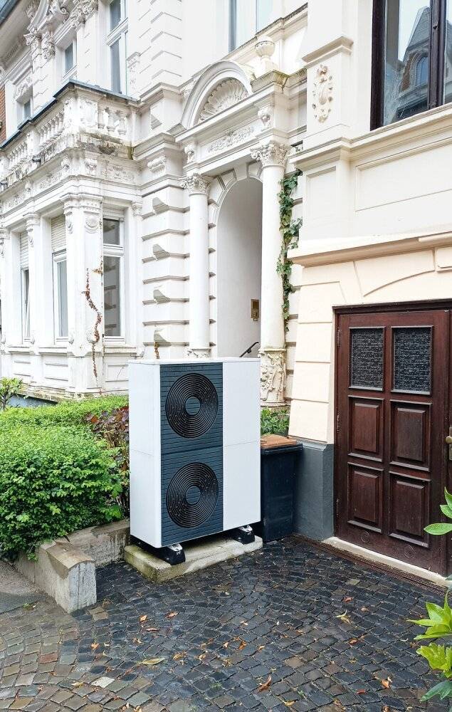 Wärmepumpe vor einem Mehrfamilienhaus.