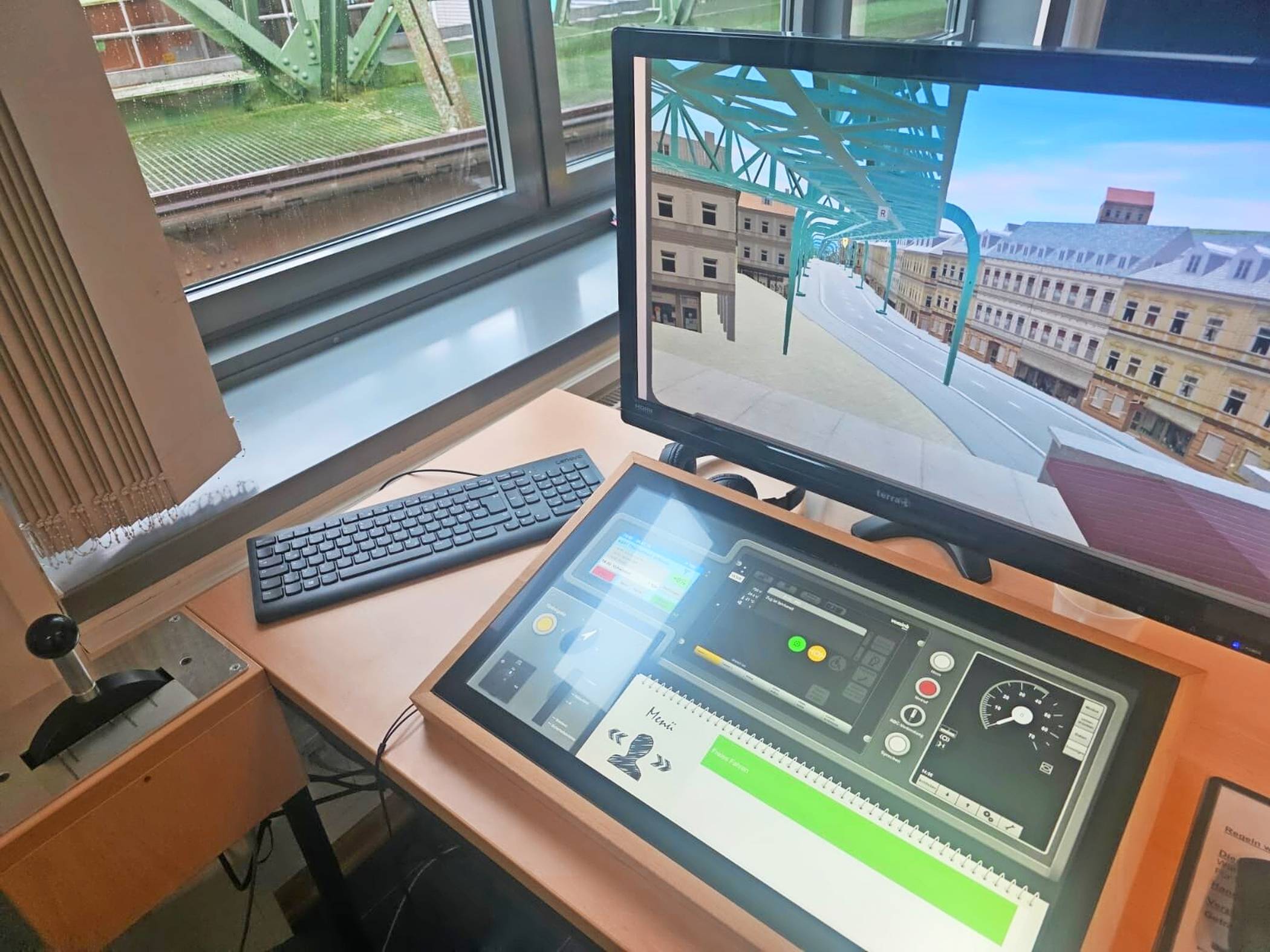 Der Schwebebahn-Simulator mit Hebel, Bildschirm und digitaler Steuerkonsole. Die Grafik erinnert an die der Playstation 1 aus dem Jahr 1994, erfüllt aber ihren Zweck.   