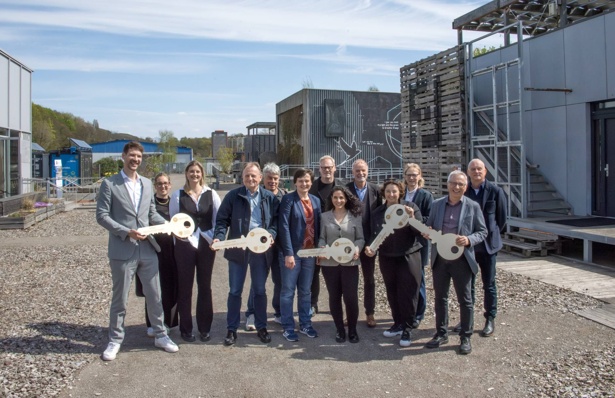 Symbolische Schlüsselübergabe: Mit den neuen Hauseigentümerinnen und -eigentümern freuten sich unter anderem die Projektverantwortlichen Dr. Katharina Simon (6.v.li.), Prof. Karsten Voss (5.v.r.) und Uni-Rektorin Prof. Birgitta Wolff (3.v.re.).