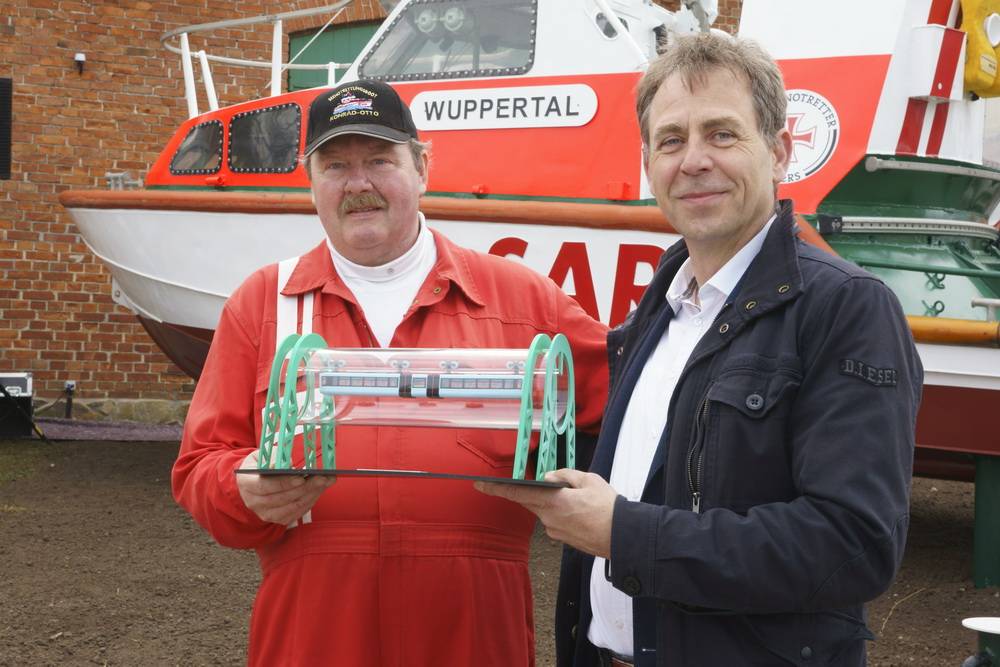  Wuppertals Marketing-Chef Martin Bang übergibt ein Modell der weltberühmten Wuppertaler Schwebebahn an Kühlungsborns Seenotretter-Vormann Rainer Kulack. 