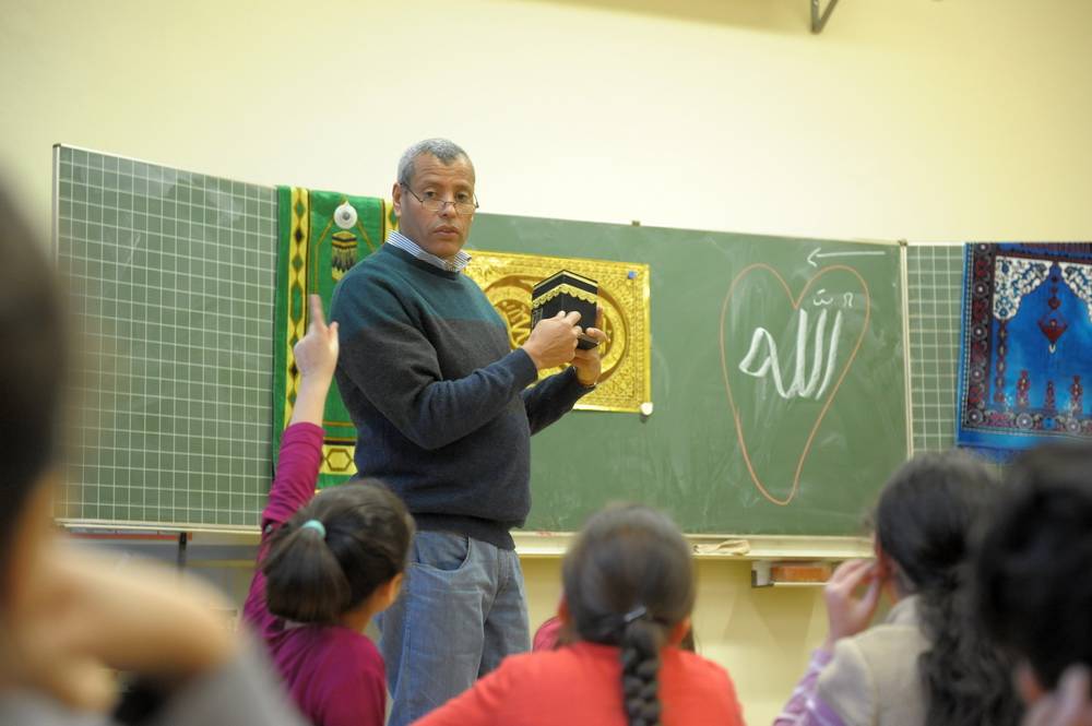  Was ist wichtig beim Gebet? Die Richtung zur Kaaba nach Mekka. Lehrer Mohamed El Kadiri zeigt hier ein Modell. Aber wo ist Mekka? Der Gebetsteppich, der im Hintergrund zu sehen ist, hat einen Kompass — und Mohamed El Kadiri ein Smartphone mit Himmelsrichtungs-Finder. 