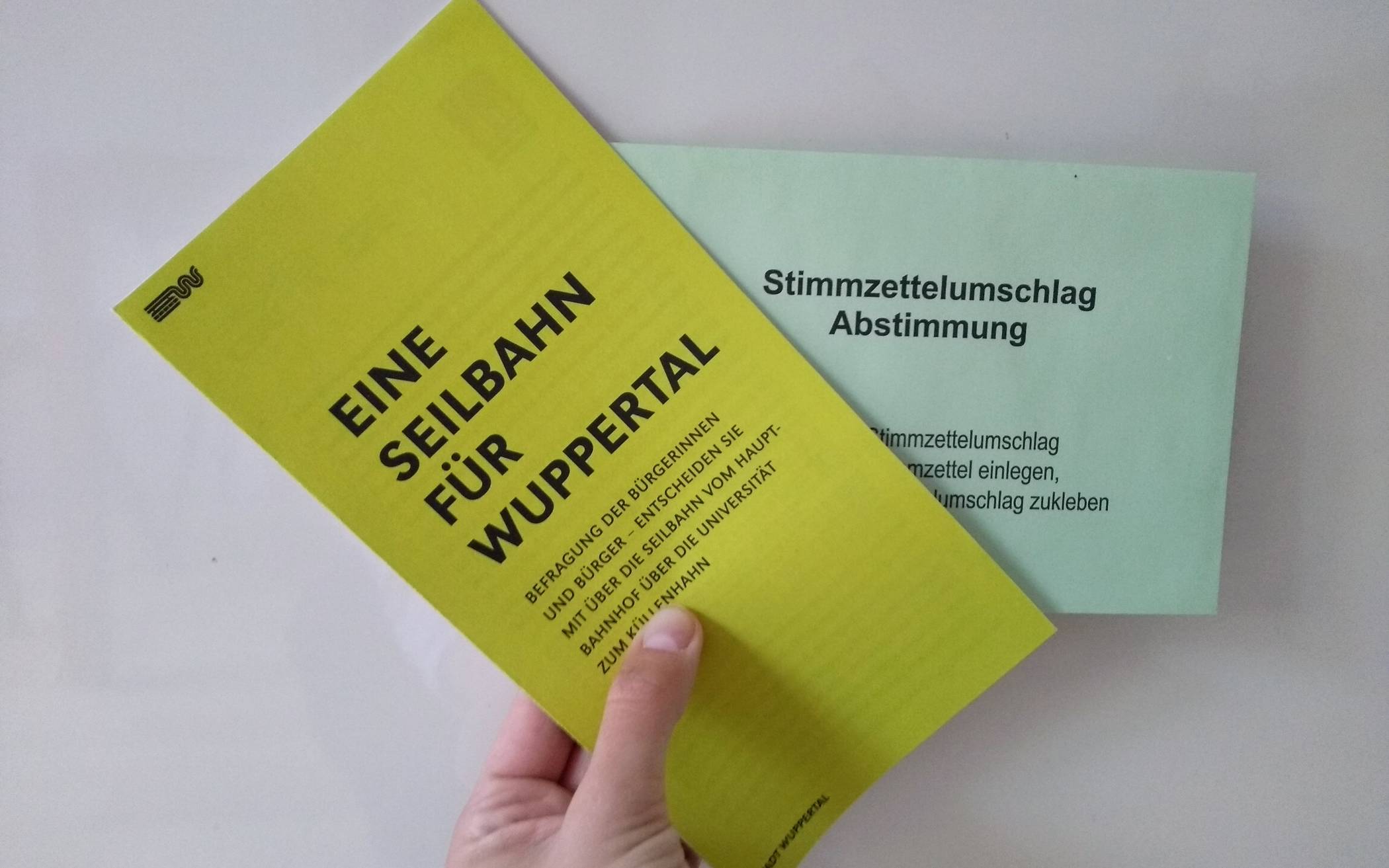  Eine gelbe Broschüre informiert zur Seilbahn, in den grünen Umschlag kommt der ausgefüllte Stimmzettel.  