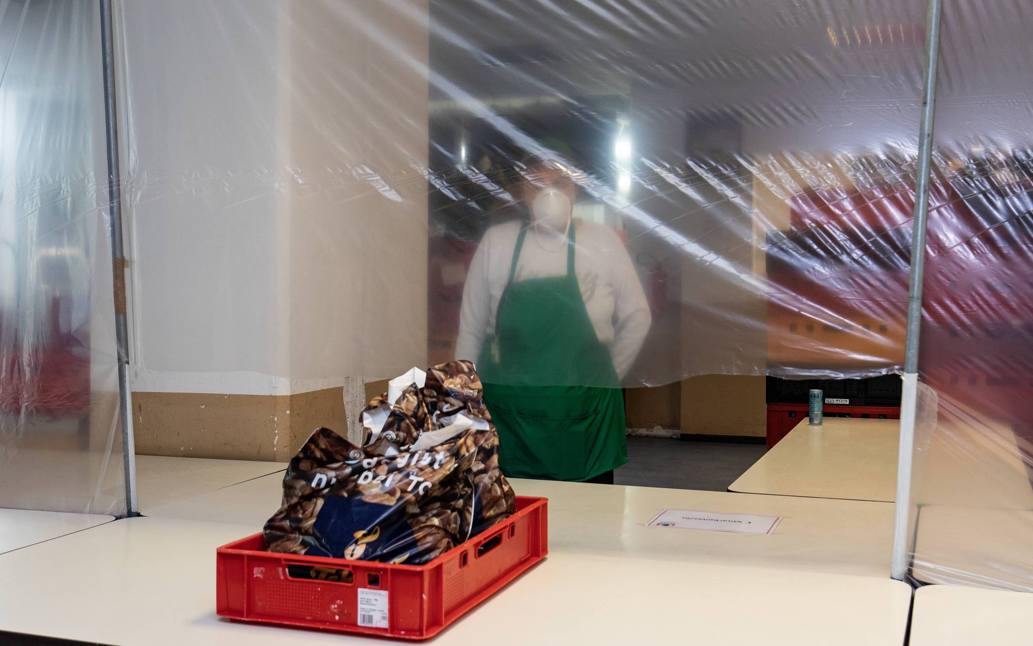 Die Wuppertaler Tafel gibt aktuel durch einen Schutz aus Folie Lebensmittelpakete an Bedürftige aus.